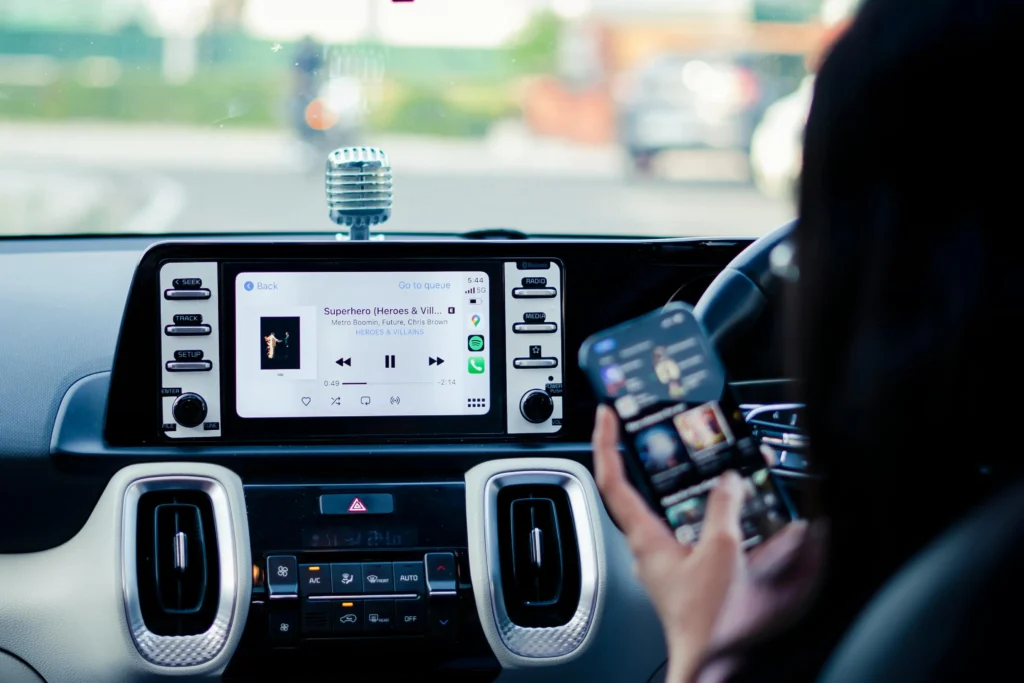 Close-up of a smart car infotainment touchscreen system connected to a smartphone displaying music playlist and navigation.