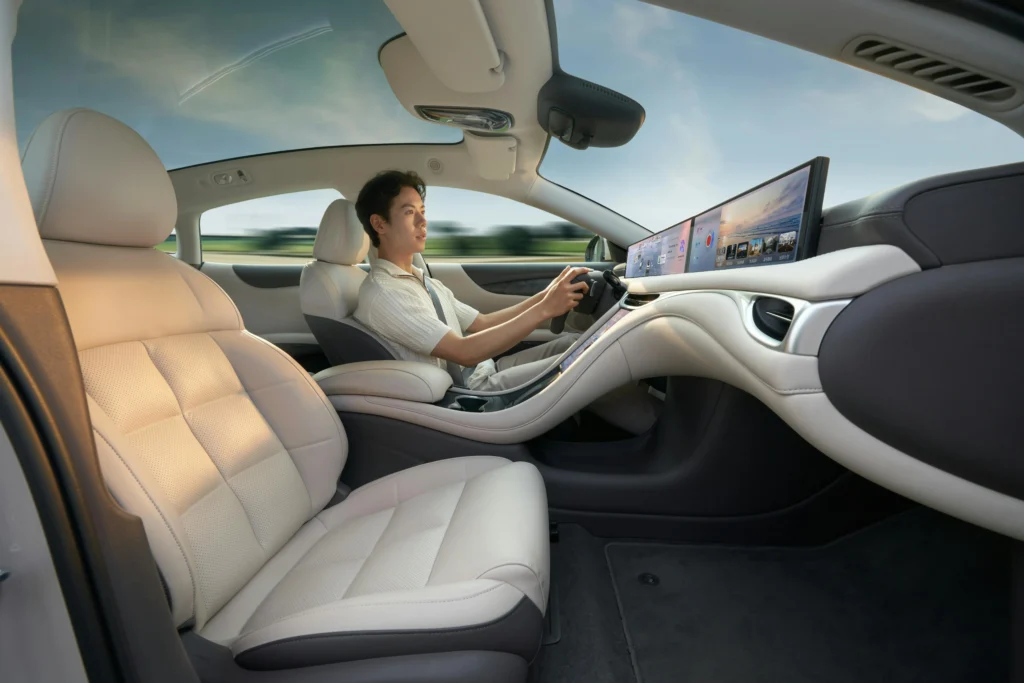 Inside view of a futuristic luxury car cabin with a massive digital dashboard screen and a panoramic glass roof with a driver.
