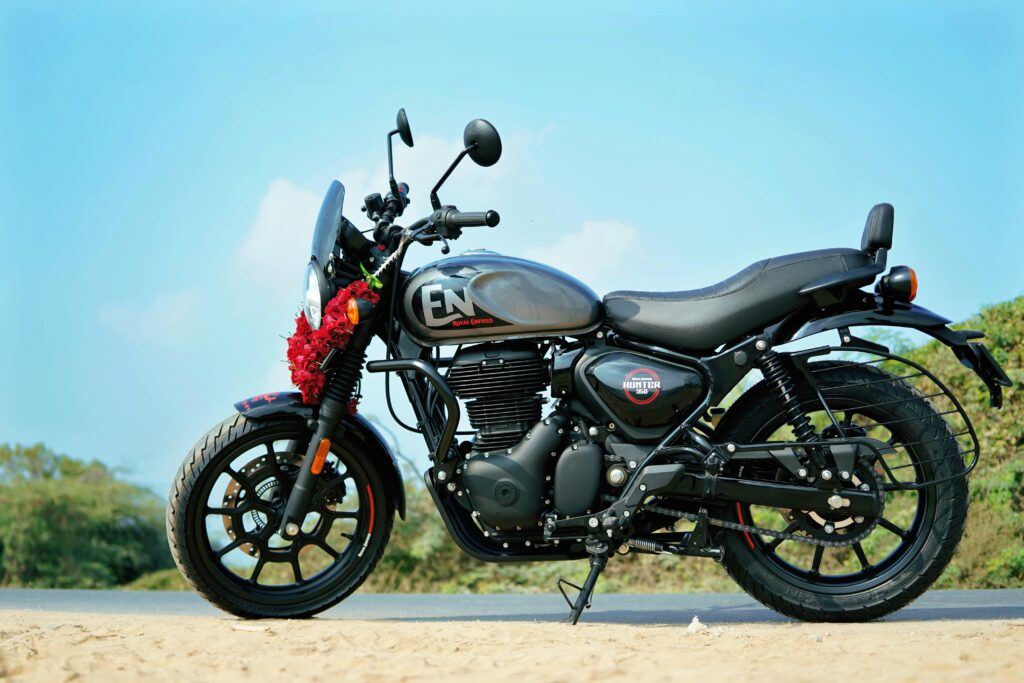 Royal Enfield Hunter 350 Dapper Grey color motorcycle with flower garland on a clean highway roadside under blue sky.