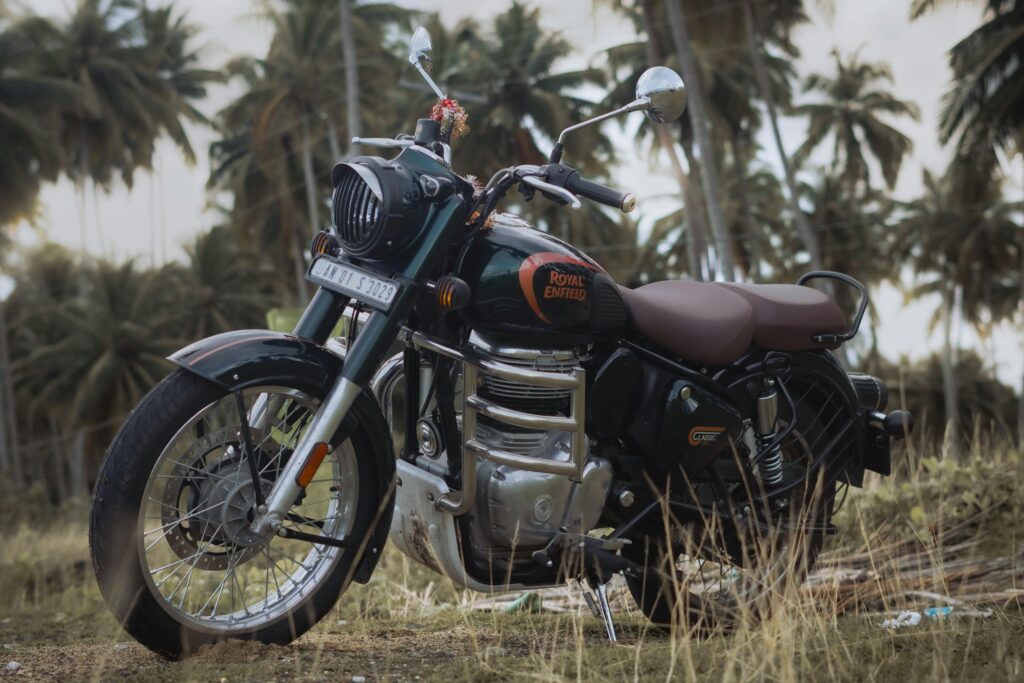 Classic Royal Enfield 350 motorcycle with chrome mirrors and brown seats parked in a scenic location surrounded by palm trees.