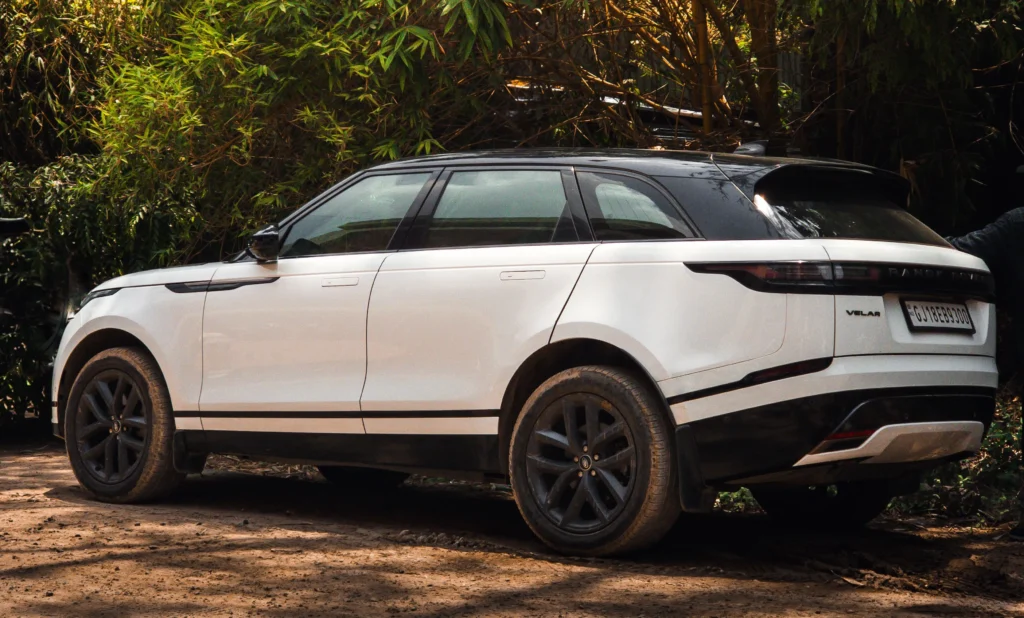 Luxury white and black Range Rover Velar SUV parked on a dirt track surrounded by dense green bamboo trees representing a premium dream car.